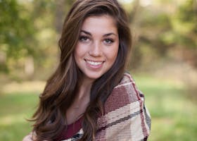 A woman smiling outdoors with a cozy plaid shawl, surrounded by nature in a sunny park.