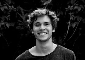 A black and white portrait of a young man smiling outdoors with natural background.