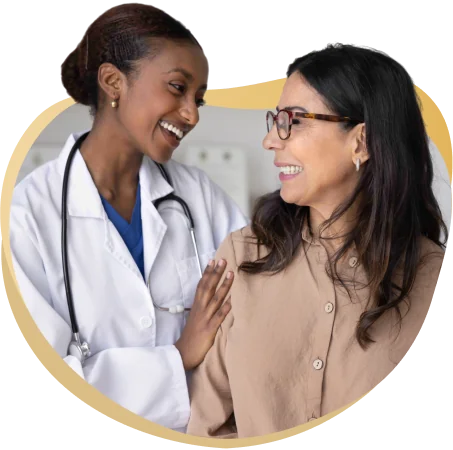 Female doctor in a white coat with stethoscope smiling and talking with a patient.