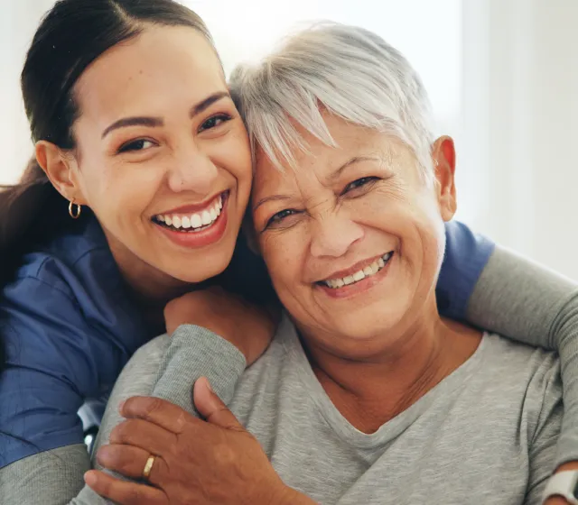 primary-care-section-img Two women, a younger and an older, smiling warmly as they hug each other in a close, affectionate embrace.